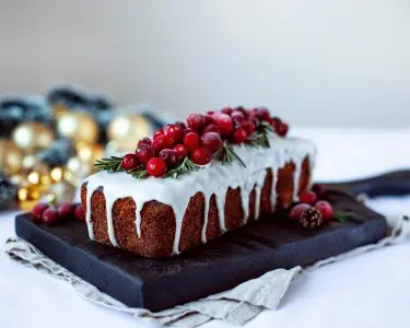Traditional Christmas cake with fruits and rosemary on white table and holiday background. Horizontal. Copy space.