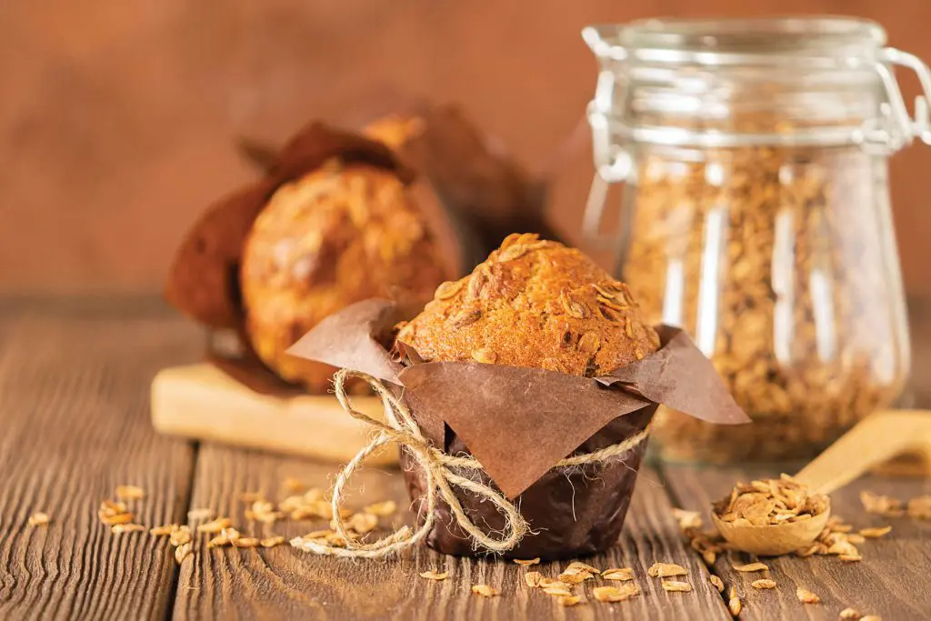 Muffins with wheat flakes in brown paper packaging close-up on a wooden background. Healthy vegan dessert. Horizontal frame. Selective focus. Copy space
