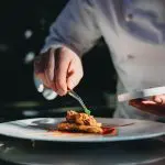 A chef is finishing the preparation of the plate. He's decorating the plate just before the serving.