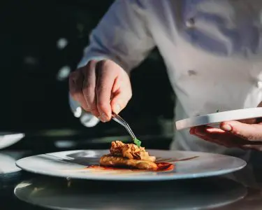 A chef is finishing the preparation of the plate. He's decorating the plate just before the serving.