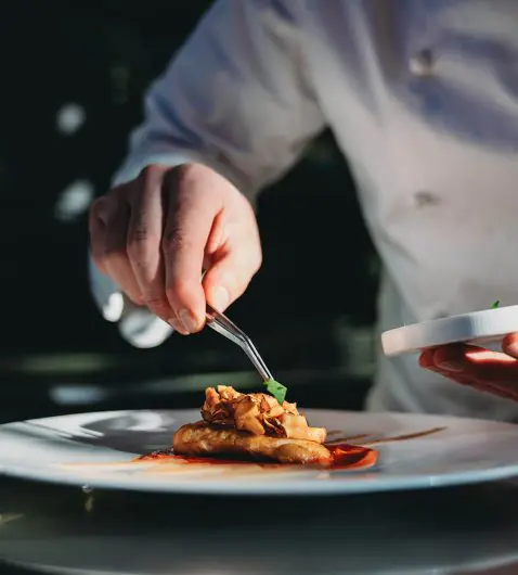 A chef is finishing the preparation of the plate. He's decorating the plate just before the serving.