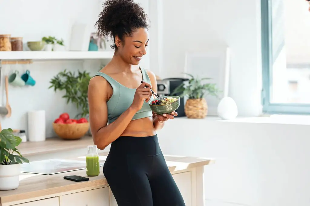 Shot of athletic woman eating a healthy fruit bowl in the kitchen at home