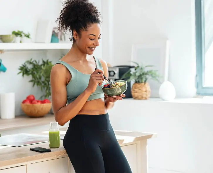 Shot of athletic woman eating a healthy fruit bowl in the kitchen at home