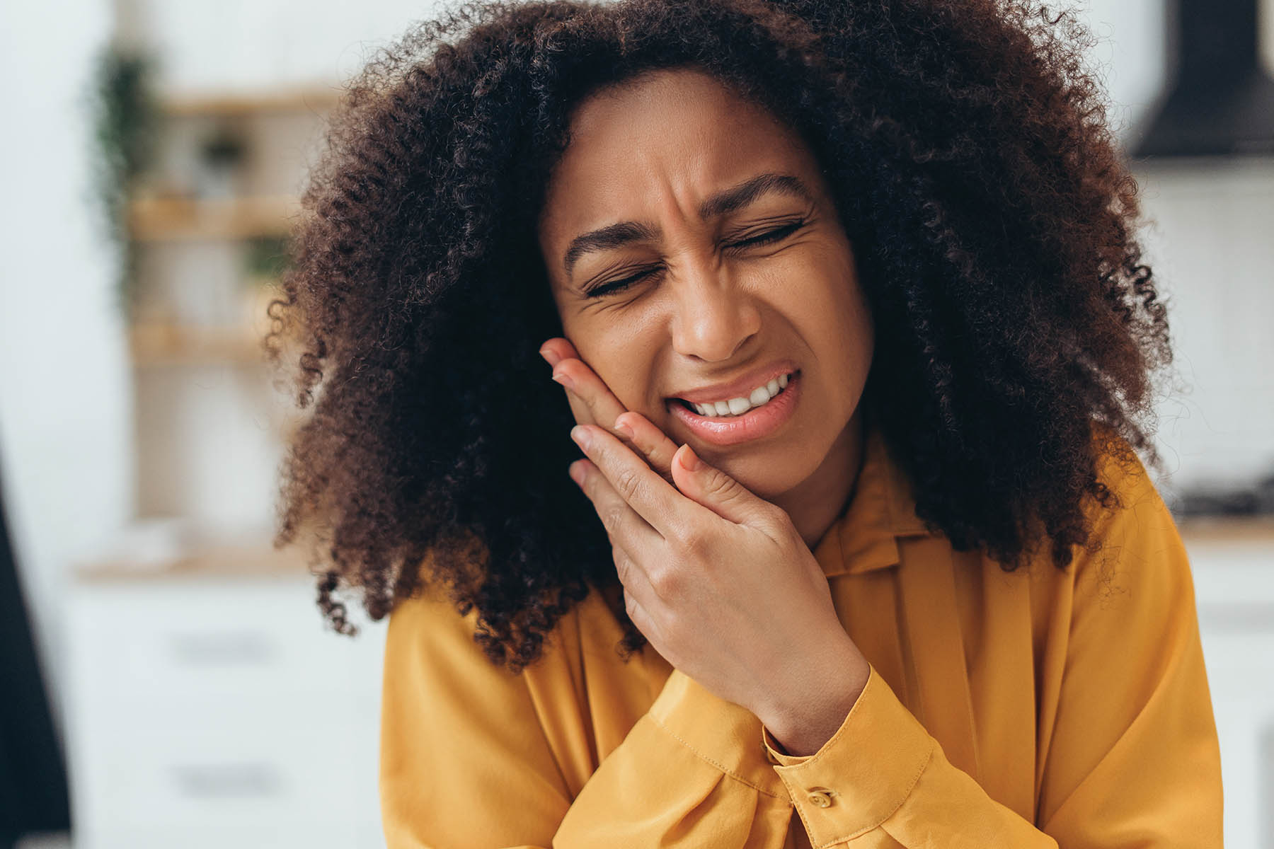 Young African American woman suffering from strong toothache touching her cheek because of acute pain at home