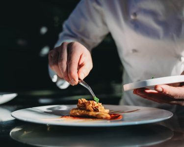 A chef is finishing the preparation of the plate. He's decorating the plate just before the serving.