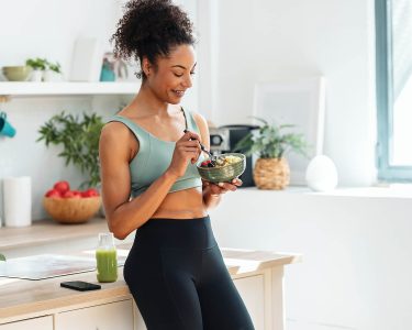 Shot of athletic woman eating a healthy fruit bowl in the kitchen at home