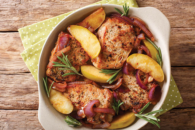 Spicy baked pork chop with green apples, onion and rosemary close-up in a baking dish on a table. horizontal top view from above