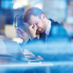 Young tired businessman sitting with his head over laptop